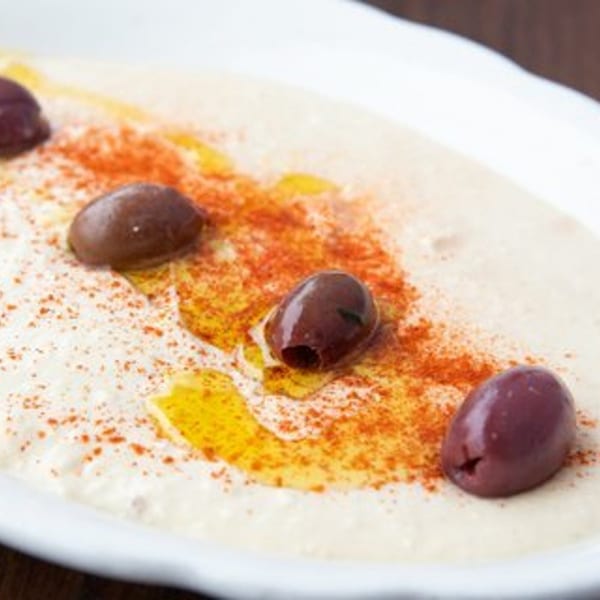 Creamy hummus topped with olive oil, paprika, and whole Kalamata olives in a white bowl.